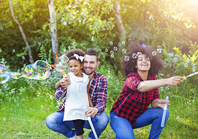 Happy family playing soap bubbles in park.